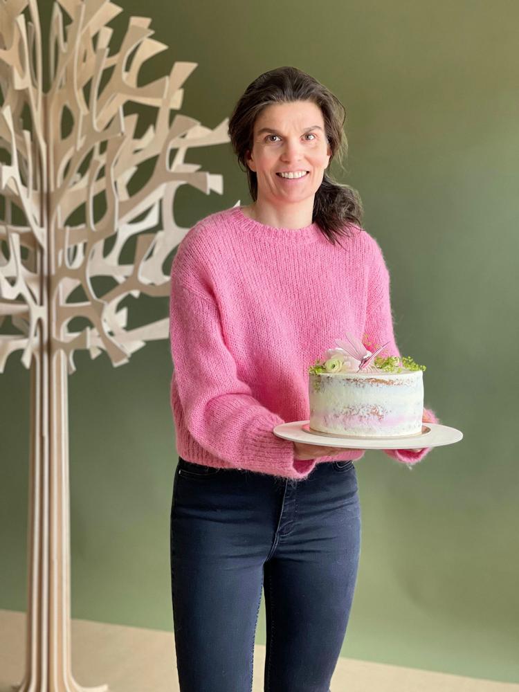 Meri holds a cake decorated with a Lovi Dragonfly. Lovi Tree 200cm on the background.