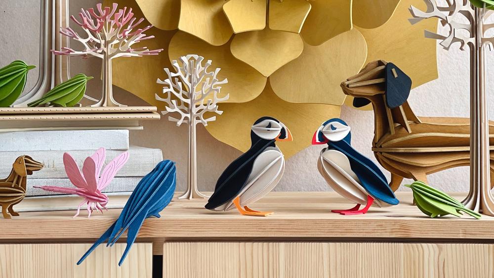 Wooden Lovi Products on sidetable. Lovi Puffins, Dachshiúnds, Swallow, Dragonfly, Birds and Trees. Frontpage image desktop.
