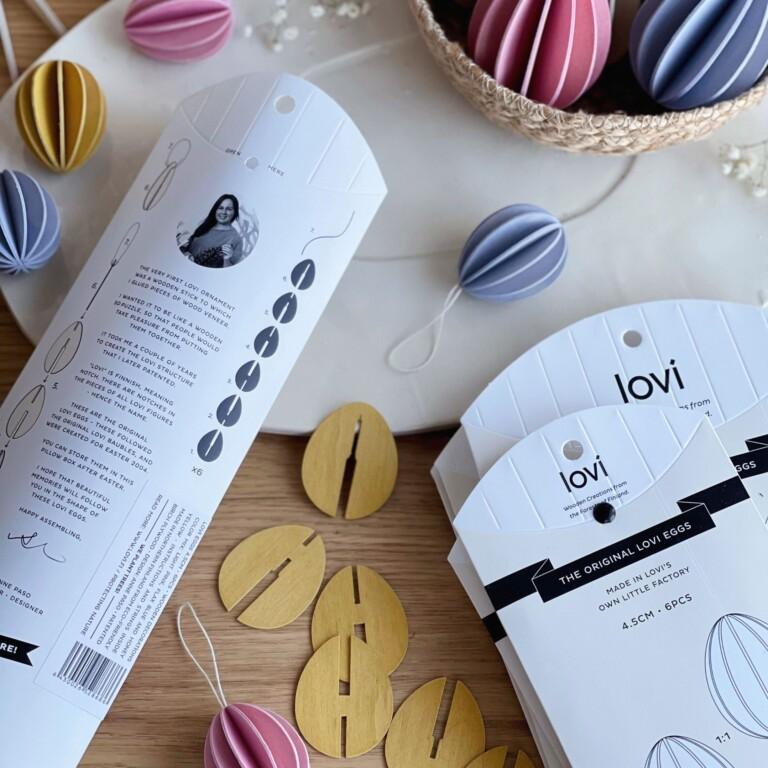 Lovi Eggs 4.5 cm, 6 pcs, wooden Easter eggs, and their package on table. Color mix (honey yellow, light pink, flax blue).